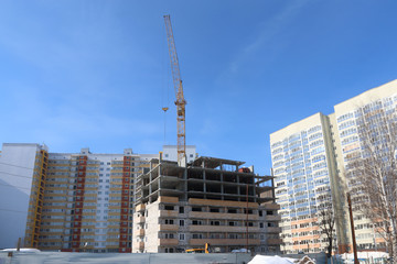 Fototapeta na wymiar Construction of multi-storey house and industrial building crane on background of blue sky