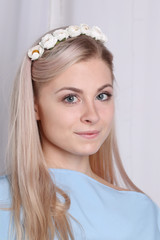 Beautiful young blonde woman with clean skin and flower wreath in her hair on grey background