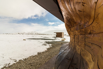 Part of the building viewpoint Snohetta, with small hut in background, winter and snow, blue sky and clouds