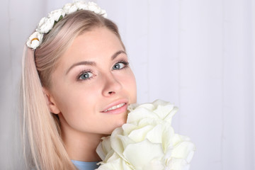 Obraz na płótnie Canvas Beautiful young blonde woman with clean skin and flower wreath in her hair holding bouquet white rose, closeup