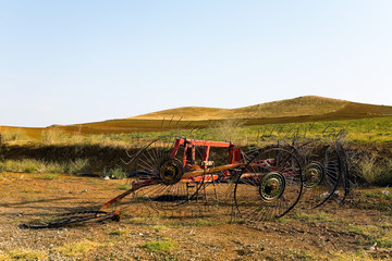 Broken agricultural machinery against the backdrop of fields and hills.