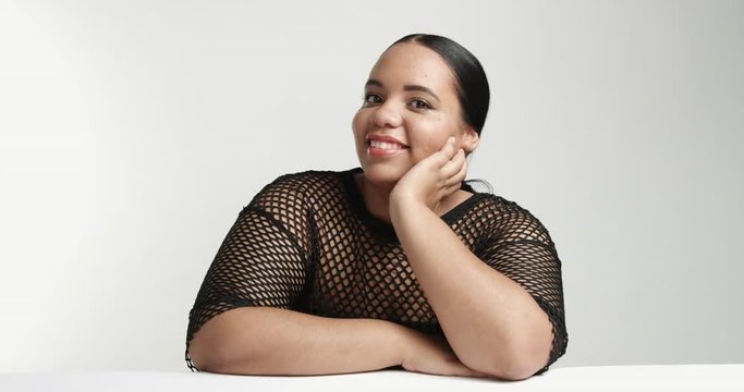 Sitting large curvy African American girl wearing a black fishnet top isolated on white. ideal skin, pretty smile portrait