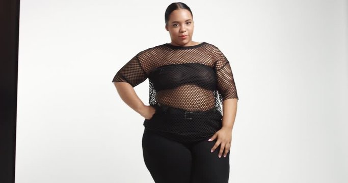 Attractive young black plus size model wearing a black fishnet top and black tight pants on white background. beauty plus size curvy model