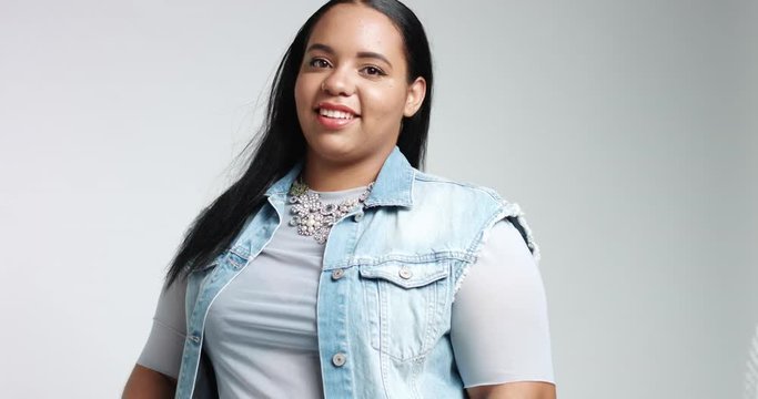 Smiling cute big African American girl in blue shirt, black pants and a denim vest isolated on white. casual style plus size model