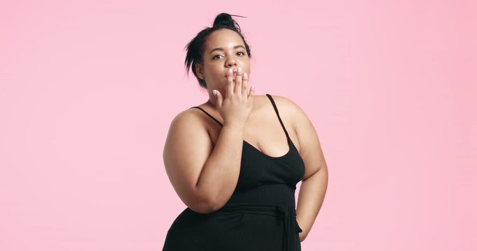 Cute plus sized curvy girl blowing a kiss on pink background