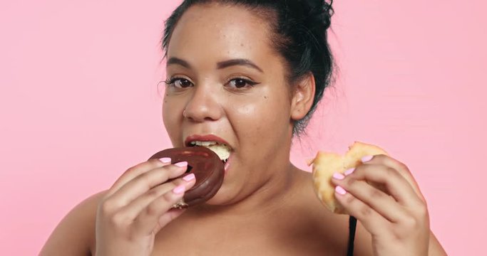 Attractive plus size model eating donuts and loving it on pink background