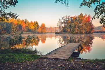 Beautiful autumn landscape. Wooden pier and colorful trees on the lake.
