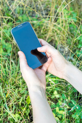 A woman's hands using a smartphone outdoors.