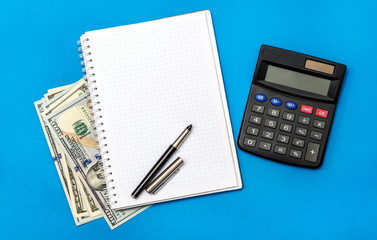 Notepad with money and calculator on a blue background. Top view. Business concept.
