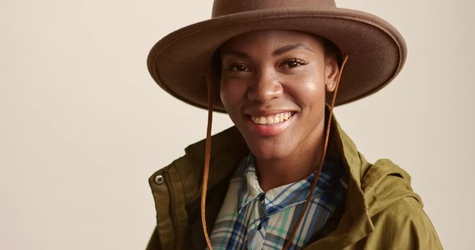 Portrait of an attractive young African woman dressed in safari hat, blue and white plaid shirt and khaki parka isolated on white