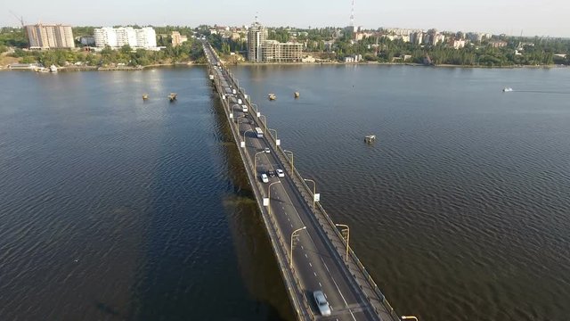 An inspiring bird`s eye view of a long modern bridge over the Southern Bug with a lot of moving cars and trucks on a sunny day in summer. The drone is flying along the bridge.The skyscape is fine