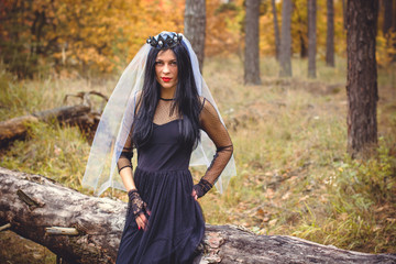 Halloween Witch with magic lights in dark autumn forest. Beautiful young european or american woman in black Gothic dress.Halloween party at city, decor and design for party, mysterious lady in woods