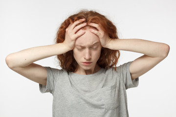 Upset unhappy redhead female squeezing head with hands, suffering from headache. People, stress, tension and migraine concept