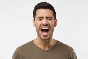 Closeup portrait of screaming with closed eyes crazy young man isolated on gray background