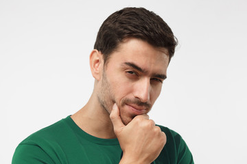 Close up portrai of suspicious man in green t-shirt, trying to read your thoughts, isolated on grey...
