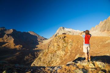 Obraz premium One person looking at view high up on the Alps. Expasive landscape, idyllic view at sunset. Rear view.