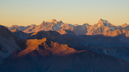 Fototapeta na wymiar Sunset over the Alps. Colorful sky, high altitude mountain peaks with glaciers, Massif des Ecrins National Park, France. Telephoto view from distant.