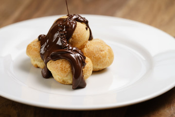pour chocolate on profiteroles on plate closeup