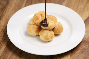 pour chocolate on profiteroles on plate closeup