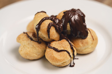 profiteroles covered with black chocolate on plate closeup