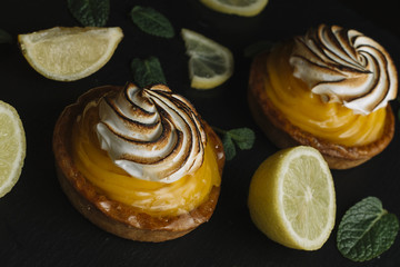 Lemon pie on the table with citrus fruits. Traditional french sweet pastry tart. Delicious, appetizing, homemade dessert with lemon cream. Copy space, closeup. Selective focus. Toned