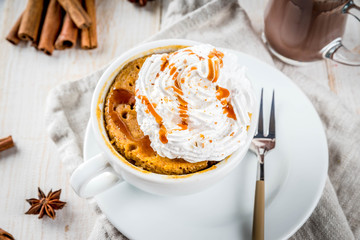 Recipes with pumpkins, fast food, microwave meal. Spicy pumpkin pie in mug, with whipped cream, ice cream, cinnamon, anise. On white wooden table, with cup of hot chocolate. Copy space