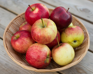 Fresh red yellow apples  in wicker plate on wooden table. Concept for seasonal fruits, autumn harvest and agriculture.