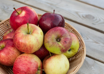 Fresh red yellow apples  in wicker plate on wooden table. Concept for seasonal fruits, autumn harvest and agriculture.