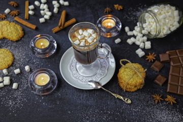 Close up of hot chocolate with marshmallows into glass. Beautiful background with candles, illicium, homemade cookies