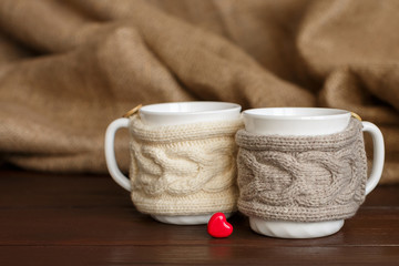 Love background, two cups of coffee with knitted cup holder near heart for valentine's day. Copy space for love text. Merry christmas concept