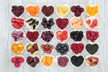 Food for healthy living with fruit, grains, vegetables and pulses in heart shaped dishes on rustic wood background. Health foods high in antioxidants, anthocyanins, vitamins and minerals.