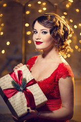 Fototapeta premium Brunette woman in red dress in luxury interior. Christmas tree. Presents and gift boxes under it. New Year decorations.