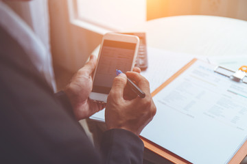 business man using smart phone working with documents on his desk