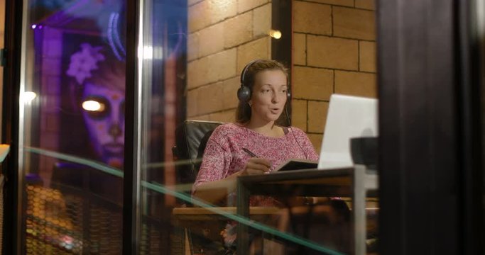 woman using laptop and headset communicating while sitting in cafe