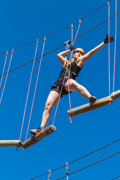 young woman in a helmet with insurance in an adventure climbing park walks by a rope simulator against a blue sky. training mountaineers in the mountains. leisure in nature. sports streets