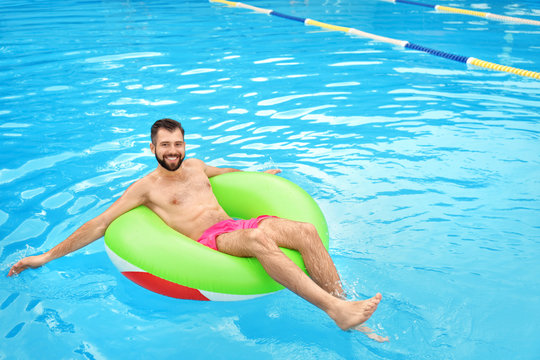 Handsome young man with inflatable ring relaxing in blue swimming pool