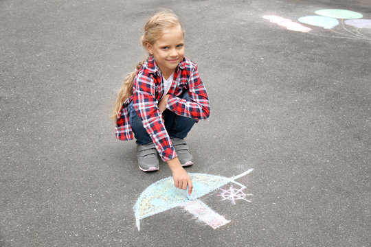 Little girl drawing ship with chalk on asphalt