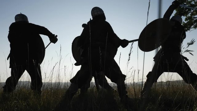 Silhouettes of Vikings warriors fighting with swords, shields. Contre-jour