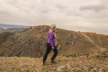 A girl in a lilac jacket walks in the mountains, an autumn forest with a cloudy dayю. Free space for text