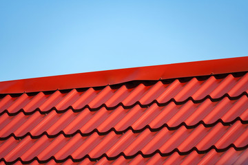 Fragment of red a metal tile roof a background of  blue sky