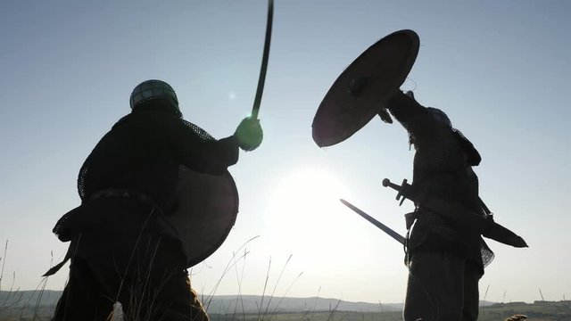 Silhouettes of Vikings warriors fighting with swords, shields. Contre-jour