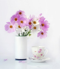 Pink flowers in a white vase and a cup of coffee near it on a white background