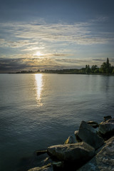 Golden sunrise over tranquil lake, dramatic clouds and sky. The golden rising sun shining from behind clouds over the horizon of calm Lake Balaton, Hungary.