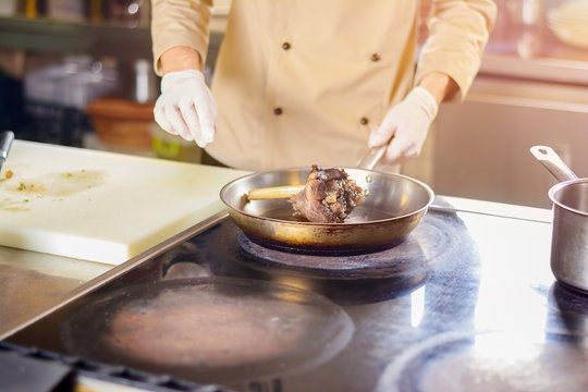 Chef frying shanks of lamb in frying pan. Chef in restaurant cooking the meat. Preparation of dish with lamb boiled leg.