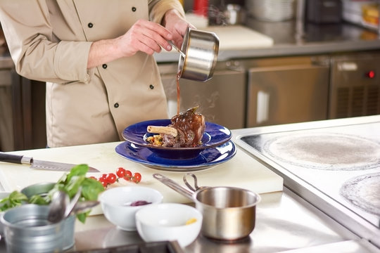 Chef pouring sauce on lamb shank. Male chef pouring with sauce fresh cooked beef shanks at european restaurant.