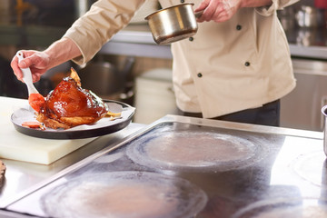 Chef processing lamb shank with sauce. Male chef at restaurant kitchen polishing with red sauce shank of lamb.