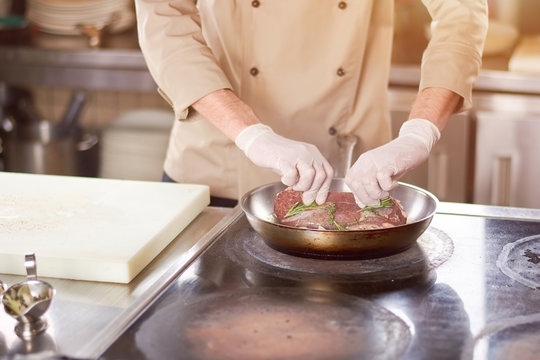 Chef putting on meat on frying pan. Close up cook hands putted meat in frying pan. Male chef cooking meat at work.