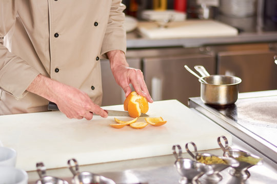 Chef cleaning orange from peel. Male chef at work, kitchen.