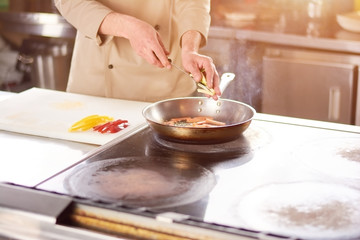 Male hands adding pepper to frying pan. Chef at professional kitchen cooking vegetables.