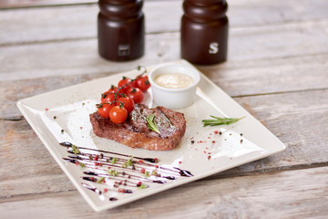 Fototapeta na wymiar Appetizing ribeye steak sprinkled with spices. Ribeye steak with sauce from madagascar pepper. Delicious ribeye steak served with cherry tomatoes and rosemary.
